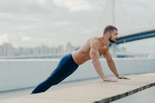 Athlete guy stands in plank pose does push up exercise outdoor breathes fresh air has strong body and naked torso motivation in staying fit and healthy leads active lifestyle. Sports training concept photo