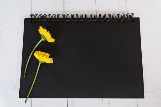 Black note book flat lay with sunflowers on wooden desk. Directly above. photo