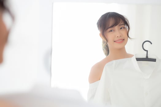 Young asian woman smiling with clothes trying on dress up fitting with modern and looking reflection mirror in the room, girl choose clothes fashion with happy and cheerful, lifestyle concept. photo