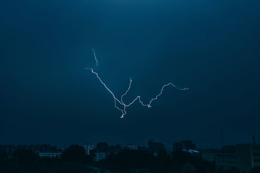 Lightning in sky over city. Bright flashes on dark night. Thunderclouds and electricity discharges in  atmosphere. photo