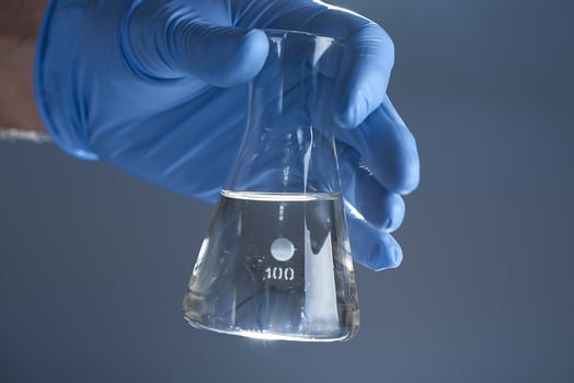 A hand in a medical glove holds a laboratory flask of liquid on a gray background. The concept of a chemical laboratory. photo