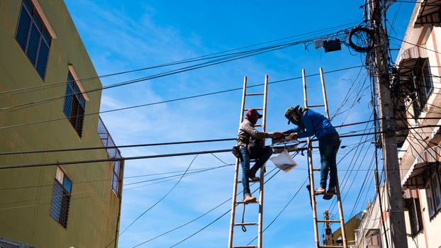 Low angle view of 2 technicians on wooden ladder are working to install telephone wires on electric pole against  the old facade and blue sky background photo