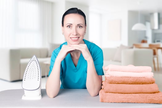 Beautiful young woman leaning on ironing board with iron and towels looking at camera and smiling while ironing clothes at home. Blurred background Home interior. Soft focus. photo