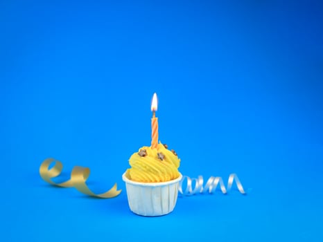 Sweet bright yellow cupcake with bow candle on blue background with copy space. Happy birthday party photo