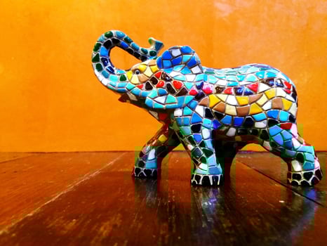 Colorful of elephant mosaic statue on the wooden table with orange wall background or wallpaper photo