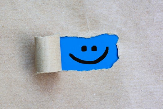Smiley face on torn hole in the sheet of brown paper on blue background. photo
