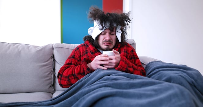 sick man is holding a cup while sitting on couch photo