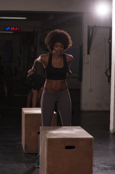 black female athlete is performing box jumps at gym photo