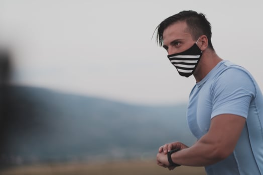 Fitness man in wet sporty clothes wearing black protective face mask running outdoors in the city during coronavirus outbreak. Covid 19 and physical jogging activity sport and fitness. New normal photo