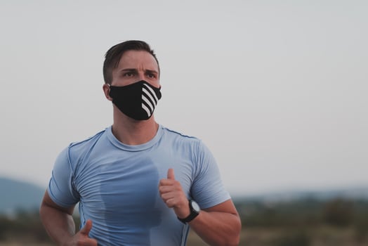 Fitness man in wet sporty clothes wearing black protective face mask running outdoors in the city during coronavirus outbreak. Covid 19 and physical jogging activity sport and fitness. New normal photo
