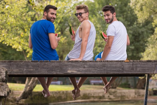 men enjoying watermelon while sitting on the wooden bridge photo