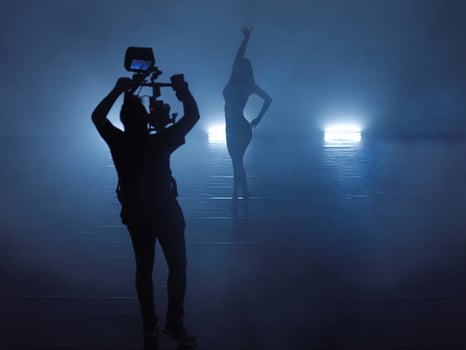 Professional videographer with gimball video slr recording video of female athletic dancer in a dark environment photo