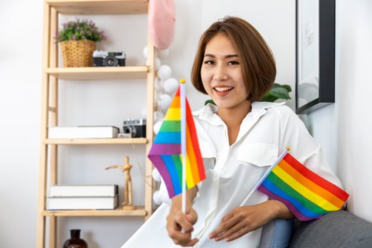 Asian girl holding LGBTQ rainbow flag in her bed room for coming out of the closet and pride month celebration to promote sexual diversity and equality in homosexual orientation concept photo