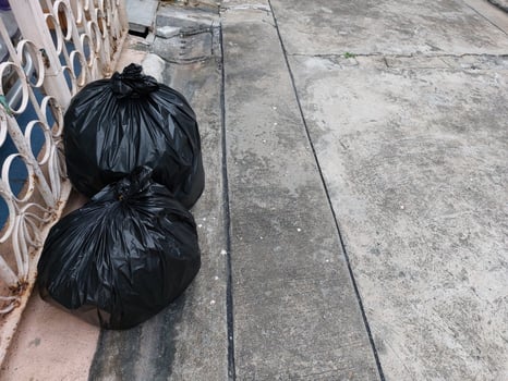 Two black trash bags were placed on the left side of the fence on the village road. photo