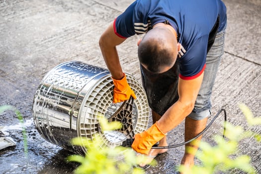 Bangkok Thailand - 6 June 2022. Handyman is washing a washing machine by removing the drum and washing it with high-pressure hose. Person wearing orange gloves while working skillfully. photo