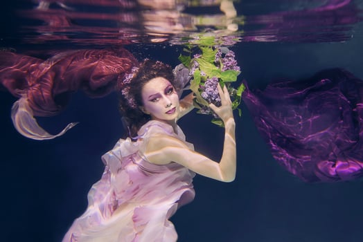 woman with lilac bouquet in colorful clothes on the dark background swimming underwater photo