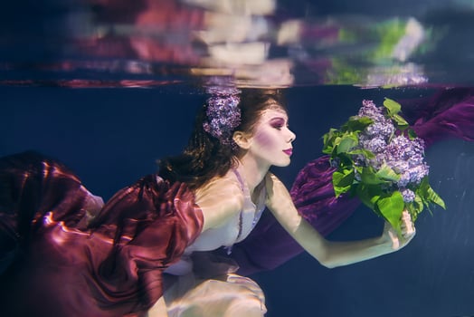 woman with lilac bouquet in colorful clothes on the dark background swimming underwater photo