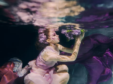 woman with lilac bouquet in colorful clothes on the dark background swimming underwater photo