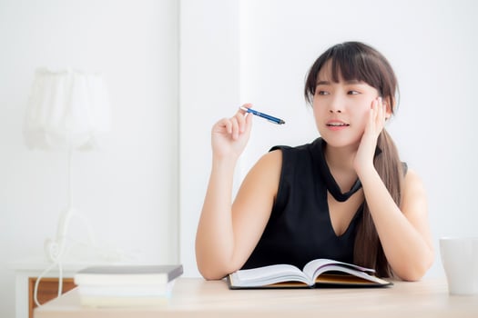 Young asian woman writer smiling thinking idea and writing on notebook or diary with happy on desk office, lifestyle of asia girl is success, female planning working, education and business concept. photo