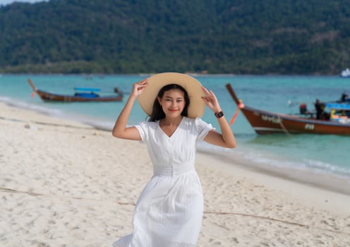 portrait of attractive Asian woman in white dress and wide brim hat smiling with happiness on blue sea beach photo