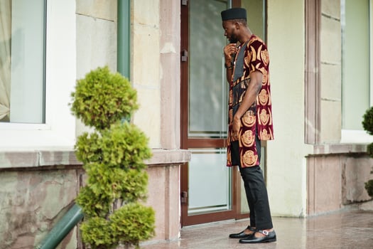African stylish and handsome man in traditional outfit and black cap standing outdoor. photo