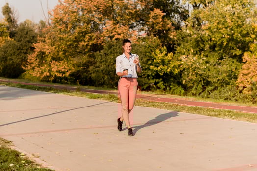 Happy young woman with coffee listening music on smartphone and walking on promenade photo