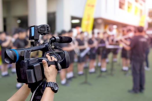 hand holding a video camera with marching band blurred background photo