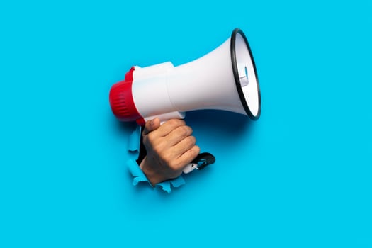 hand holds a megaphone blue background out of a torn hole in a paper background photo