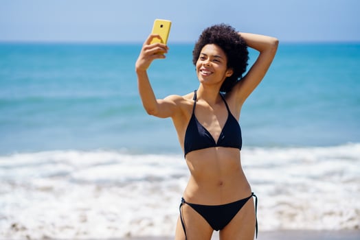 Content black woman in bikini taking selfie on beach photo
