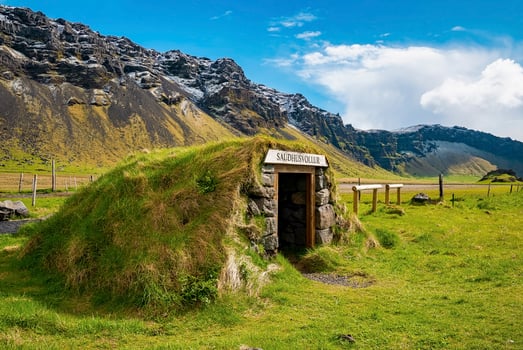 Beautiful Saudhusvollur turf shelter by mountain against blue sky photo