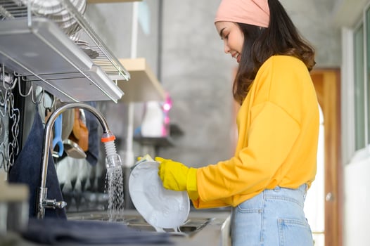 Young happy woman wearing yellow gloves washing dishes in kitchen at home photo