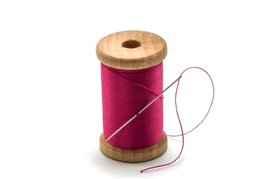 Isolated wooden spool of pink thread with a needle photo