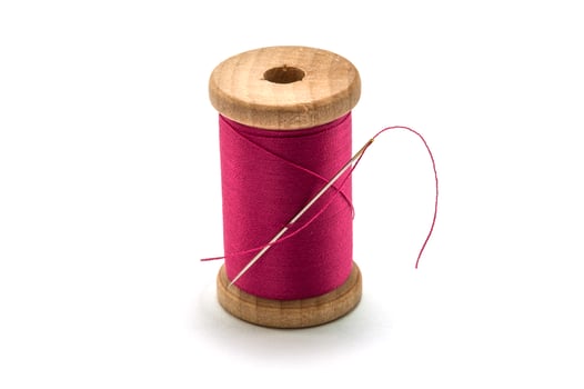 Isolated wooden spool of pink thread with a needle photo
