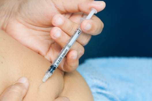 A lady is injecting insulin into her stomach. Photo is focus at syringe.