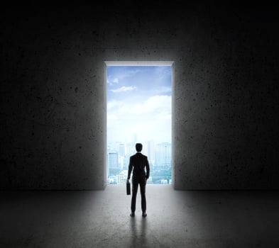 Businessman standing in front of bright big shining door in a concrete wall with a view to the city photo