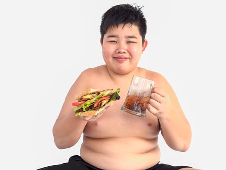 A fat boy is happily eating sandwich with soft drink photo