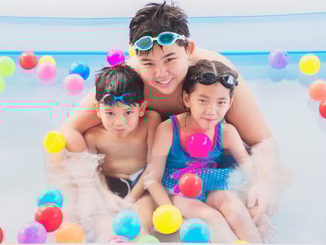 Asian brotherhood are playing in a kid water pool with colorful balls. Photo is focused at the biggest kid's face.