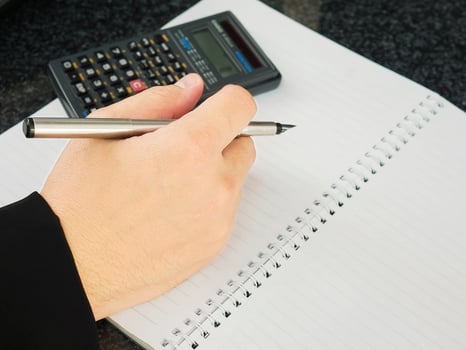 Business man is holding pen with empty note book working with calculator. Financial working concept. photo