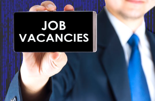 Job vacancies word on mobile phone screen in blurred young businessman hand and digital technology background photo