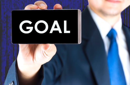 GOAL word on mobile phone screen in blurred young businessman hand and digital technology background, business concept photo