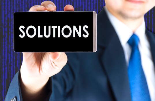SOLUTIONS word on mobile phone screen in blurred young businessman hand and digital technology background, business concept photo