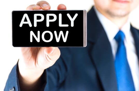 APPLY NOW, word on mobile phone screen in blurred young businessman hand over white background, business concept photo