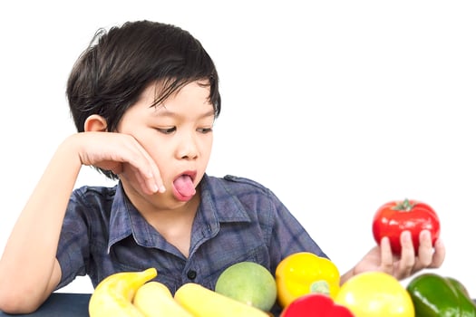 Asian boy is showing dislike vegetable expression over white background photo