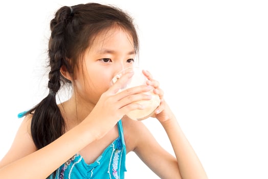 Asian girl is drinking a glass of milk over white background photo