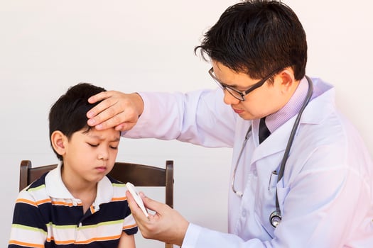 Sick Asian boy being examined by male doctor over white background photo