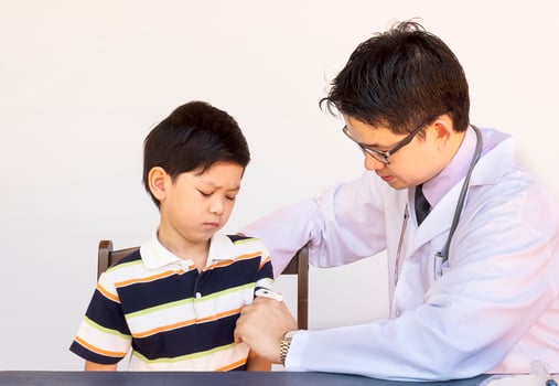 Sick Asian boy being examined by male doctor over white background photo