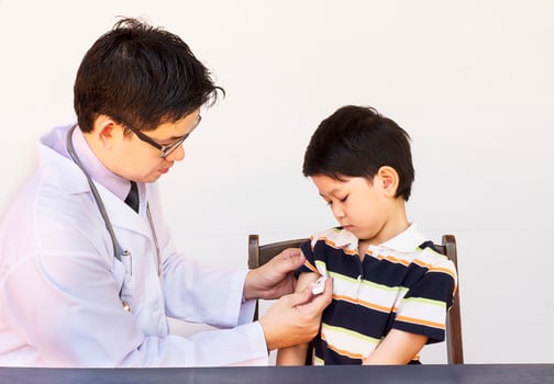 Sick Asian boy being examined by male doctor over white background photo