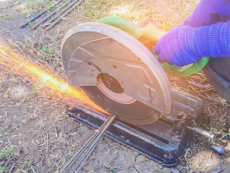 Worker's hand cutting steel rod by a machine in construction site photo