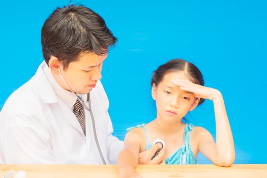 Sick Asian girl is being treated by male doctor over blue background photo