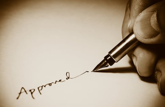 Old brown vintage vignette photo style of closeup of approved signature with fingers and pen in a dark room